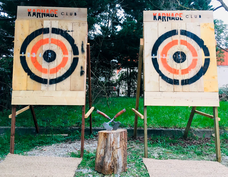 Cibles mobiles pour le lancer de haches du Karnage Club, derrière deux haches plantées dans un rondin en bois